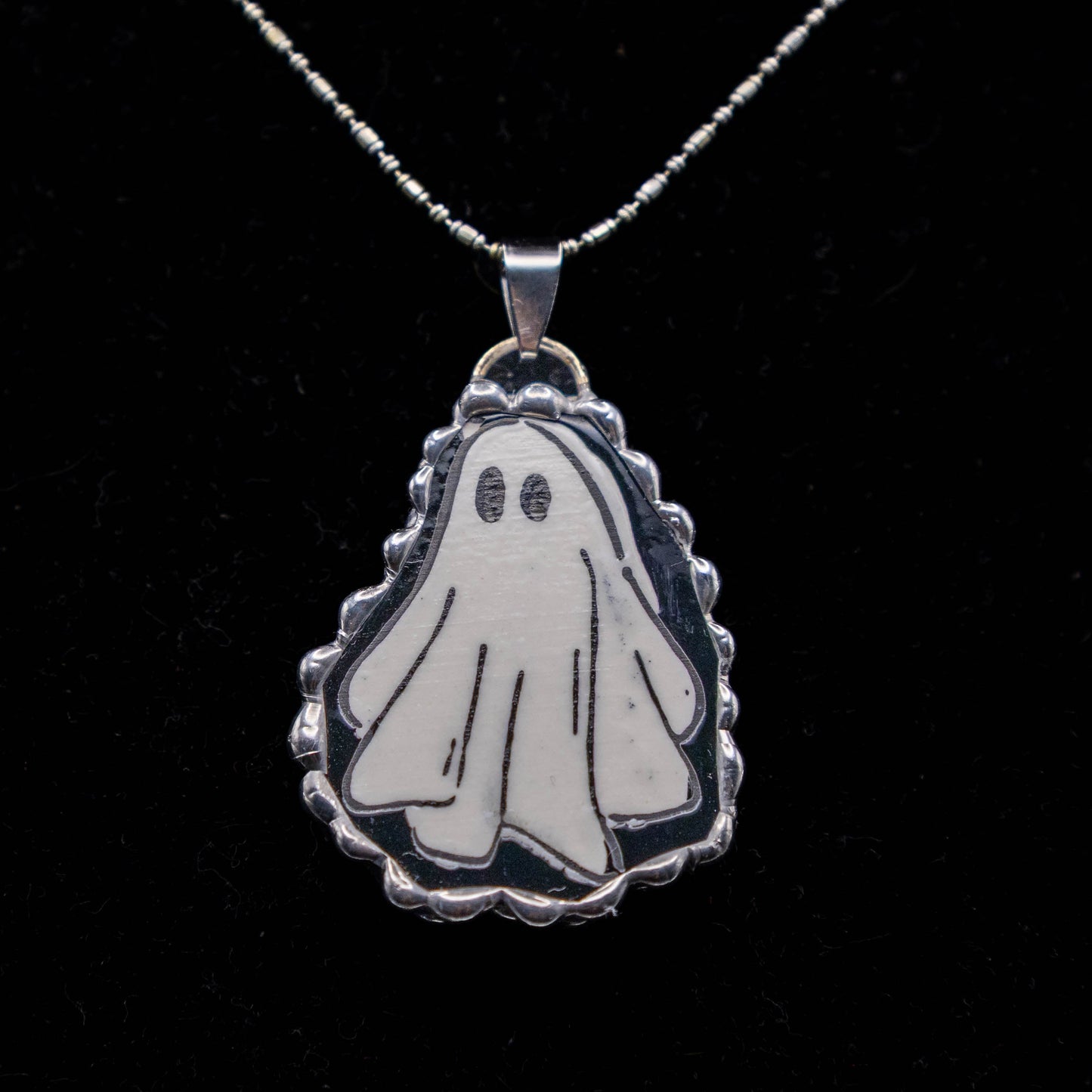 Ghost-shaped pendant on a chain against a black background