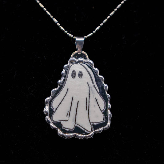 Ghost-shaped pendant on a chain against a black background